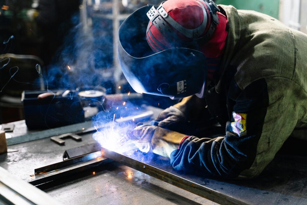 pexels-photo-2381463-2381463 A welder works on metal fabrication indoors, creating bright sparks and smoke.